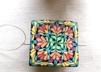 Example of a threaded needle being placed through the hole under the decorative top.